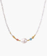 Delicate white beaded necklace with baroque pearl center, gold accents, and coral and aqua gemstones on cream background.