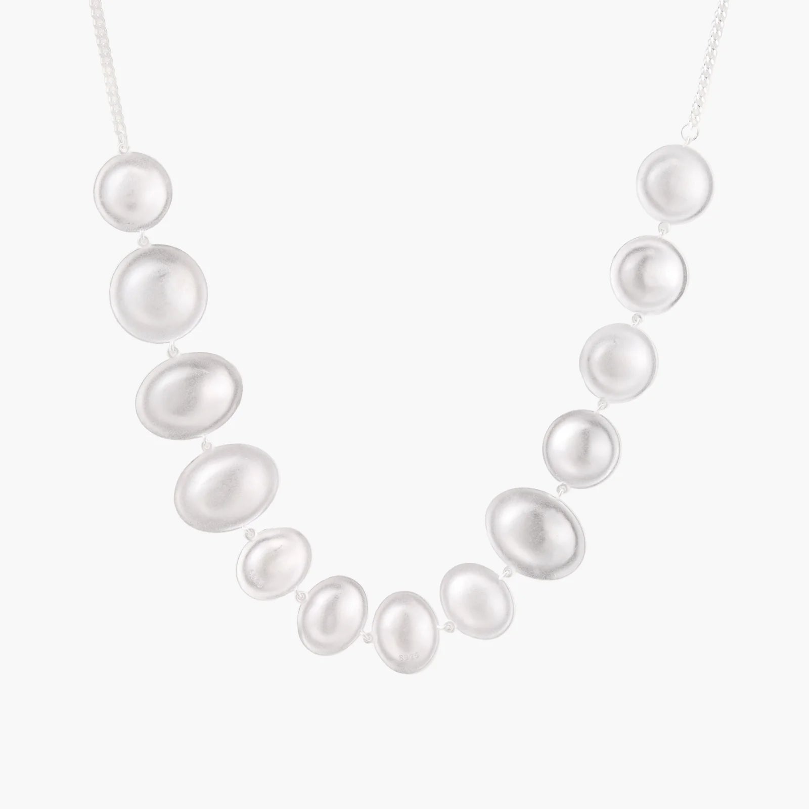 Graduated pearl-finish silver discs forming an organic bubble bib necklace on delicate chain against cream background.